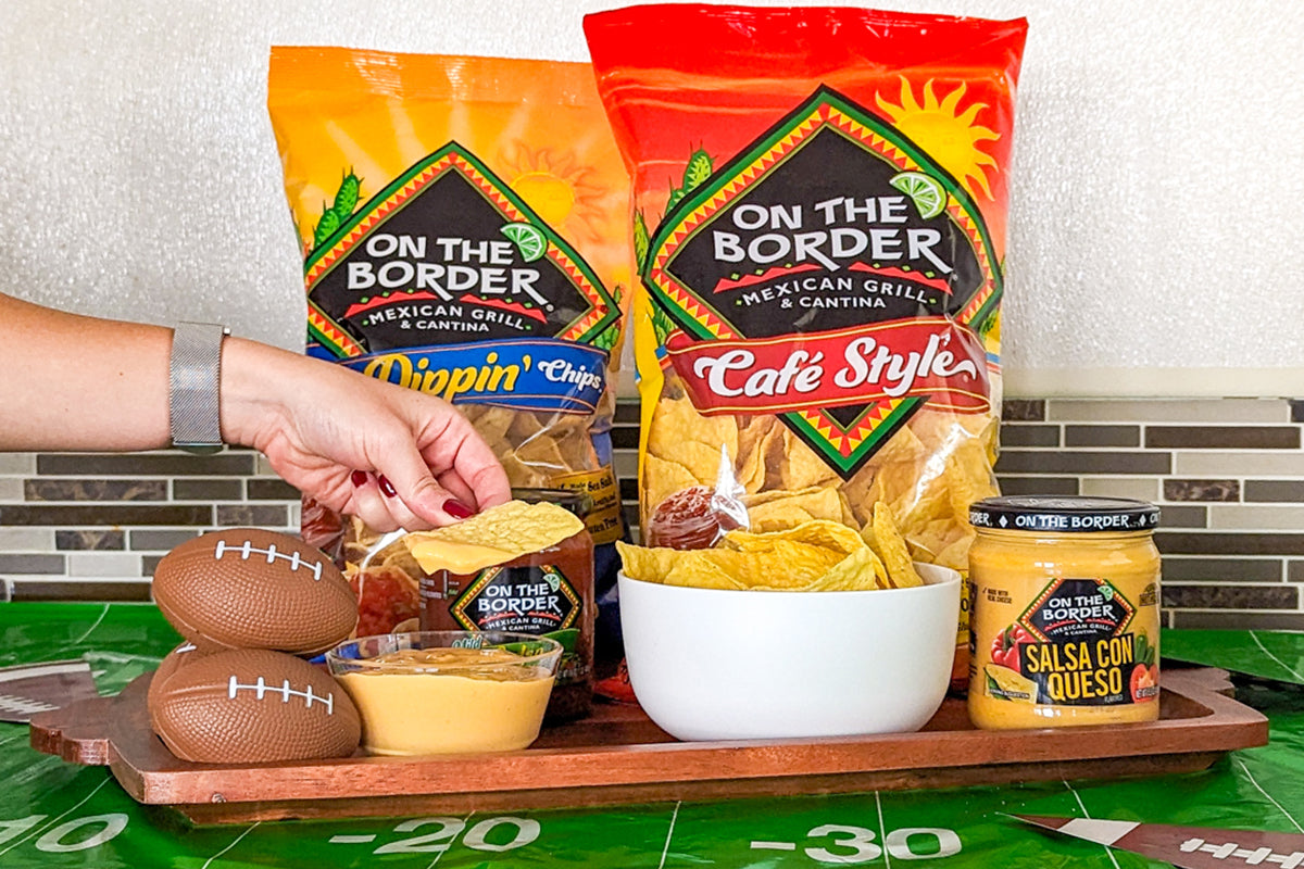 On The Border chips and salsa on a tray with a person's hand reaching for a bag.